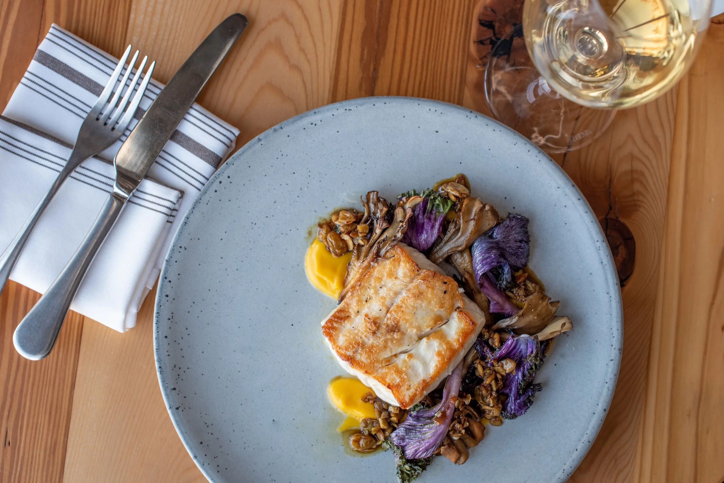 A plated fish course with seasonal vegetables at Oak & Reel